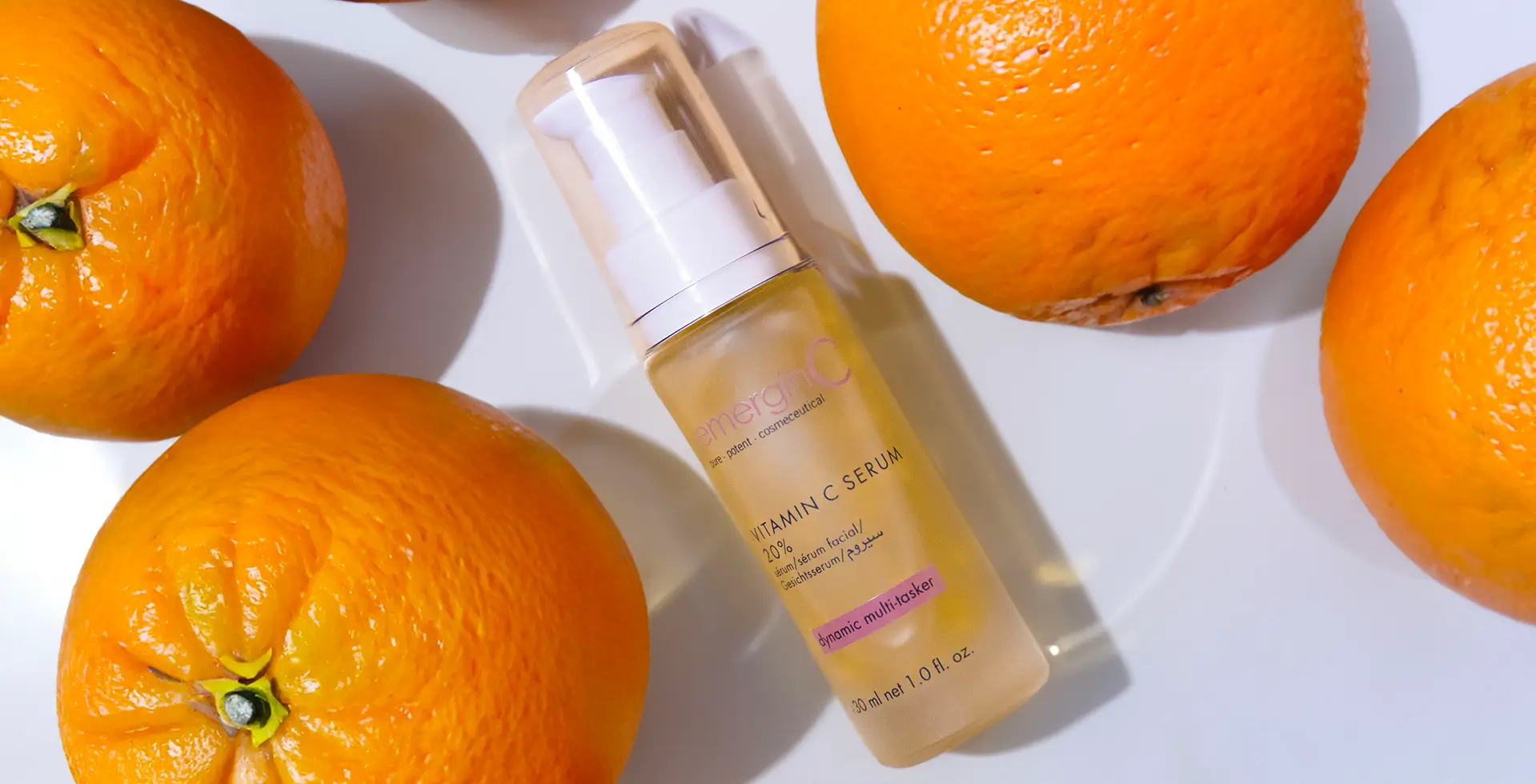 A bottle of vitamin c serum next to two oranges.